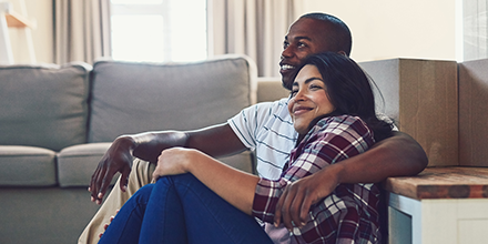 Young couple sitting on the floor of their new home, surrounded by moving boxes symbolizing starting out.