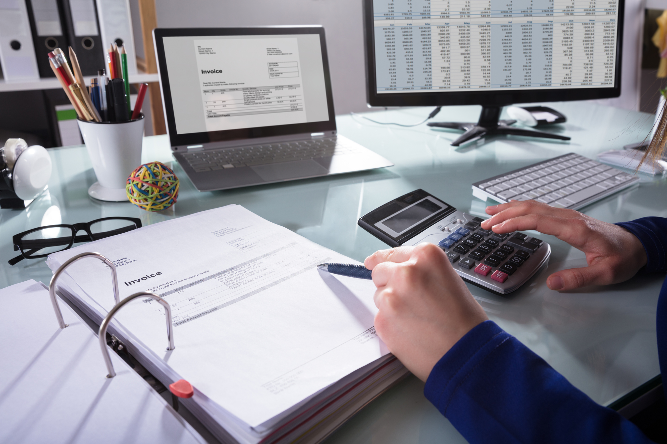 A business owner working at their desk with computer, laptop and calculator reviewing cash flow. 